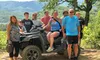 A group of people is gathered around an ATV in a scenic mountainous area, with some smiling for the camera.