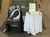 The image shows a POW/MIA memorial setup featuring a small table with a symbolic place setting, a flag, and a rose, alongside a chair draped with a POW/MIA cloth in front of a display case.