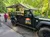 A Jeep from Smoky Mountains Jeep Tours is parked on a road beside a group of people in a lush, green wooded area.
