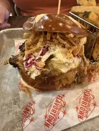 A hearty sandwich with coleslaw and crispy fried onions is served on a tray next to a basket of fries.