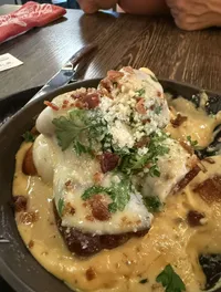 A delicious-looking dish covered in melted cheese, garnished with herbs and bacon, sits on a wooden table.