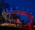 A brightly lit roller coaster track is illuminated with colorful lights against a nighttime sky.