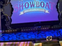 An audience is seated facing a stage with a large screen displaying 