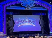 An audience is seated in front of a stage with a vibrant backdrop displaying 