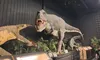 The image shows life-sized dinosaur models in a museum or exhibit setting, with a prominent, sharp-toothed dinosaur in the center.