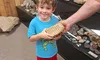 A child is holding a large fossil or rock in a museum or exhibit setting, assisted by an adult.