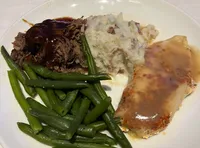 A plate of food featuring green beans, mashed potatoes, roast beef with gravy, and a glazed piece of fish.