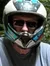 Two people wearing helmets are riding muddy ATVs on a dirt trail in a forest.