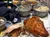 The image shows a table filled with a meal including fried chicken, mashed potatoes, corn, and other sides, set in a casual dining environment.