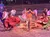Performers in vibrant Western-style costumes are energetically dancing in front of a seated audience.