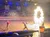 A lively arena show features performers running across a sandy stage with a flaming circle, as a large audience watches from the stands.