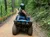 A person wearing a helmet is riding an ATV on a dirt path through a lush, green forest.