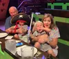 A family with two young children, one dressed as a pirate, is sitting at a table in an enclosed venue with green and brown seating.