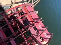 The image shows a red paddlewheel on a riverboat beside calm blue water.