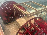 This image shows a red paddlewheel on the back of a boat, surrounded by water.