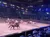 A rodeo-like show is taking place in an arena with riders on horseback herding cattle, while a large audience watches from the surrounding seats.