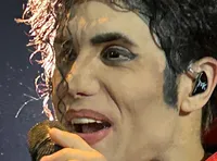 A performer wearing a red, sparkling jacket sings into a microphone while standing in an auditorium.
