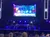 A crowd is seated in front of an illuminated stage with a screen displaying various social media icons.