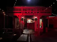 The image shows a dimly lit, Western-style saloon with a red-tinted facade, under string lights.