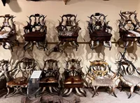 The image shows an array of chairs creatively crafted from antlers and upholstered with fur, displayed along a wall.