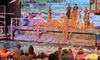 A performer is mid-air above a water-filled stage during a theatrical show with an audience watching.