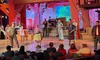 The image shows a lively stage performance in a barn-themed setting, with actors in costume and an audience watching.