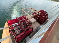 A red paddle wheel is propelling a boat across a body of water, leaving a foamy trail behind.
