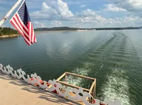 A boat with an American flag is cruising on a calm body of water under a partly cloudy sky.
