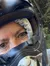 A person wearing a helmet takes a selfie while others ride ATVs on a trail in a wooded area.