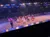Performers in colorful costumes are entertaining an audience in an arena-like setting with a horse-drawn cart in the background.