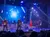 A band performs energetically on stage with colorful lighting and a dynamic digital backdrop.
