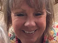 Three women are smiling for a selfie with a riverboat and body of water in the background.