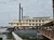 The image shows a large paddle steamer boat docked at a pier under a cloudy sky.