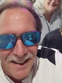 Four people are happily posing for a selfie in front of a vibrant backdrop of flowers.