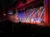 Performers are dancing on a brightly lit stage in front of an audience in a theater.