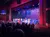 Performers dressed in red, white, and blue are on stage in front of an audience, with a large American flag backdrop and colorful stage lighting.