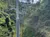 People are riding on a ski lift through a lush, green forested area under a partly cloudy sky.