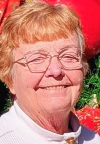 A person is standing happily in front of a large, festively decorated Christmas tree outdoors.