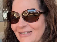 A couple wearing matching hoodies and sunglasses smiles while taking a selfie outdoors.