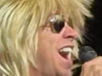 Four performers with extravagant costumes and hairstyles are singing on stage.