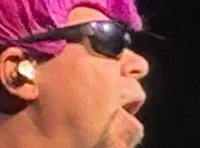 Four performers in flamboyant costumes and wigs are energetically singing on stage.