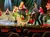 A festive stage performance featuring dancers in Christmas-themed costumes and decorations, including a sleigh and holiday lights.