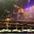 The image shows a stage set for a pirate-themed performance with actors in colorful costumes on a ship, viewed from a dinner table setting with plates and mugs.