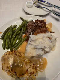 A plate of food featuring green beans, mashed potatoes with gravy, sliced roast beef in sauce, and a seasoned piece of grilled chicken.