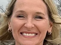 Three people are standing on a scenic overlook with a view of a lake and an American flag.