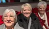 Three women are smiling while sitting in front of a backdrop of red poinsettias.