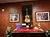 The image features a wooden display with a guitar encased in glass, flanked by framed photos on a textured wall, decorated with festive elements like a red tablecloth, pine decorations, and a small reindeer figure.