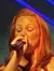 A woman in a sparkling red dress is singing on stage with a colorful geometric backdrop.