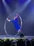 A performer in a blue outfit is balancing inside a large hoop on a stage, under dramatic lighting.