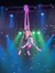 Two aerial performers are mid-air, executing a routine with silk ropes against a backdrop of stage lights.